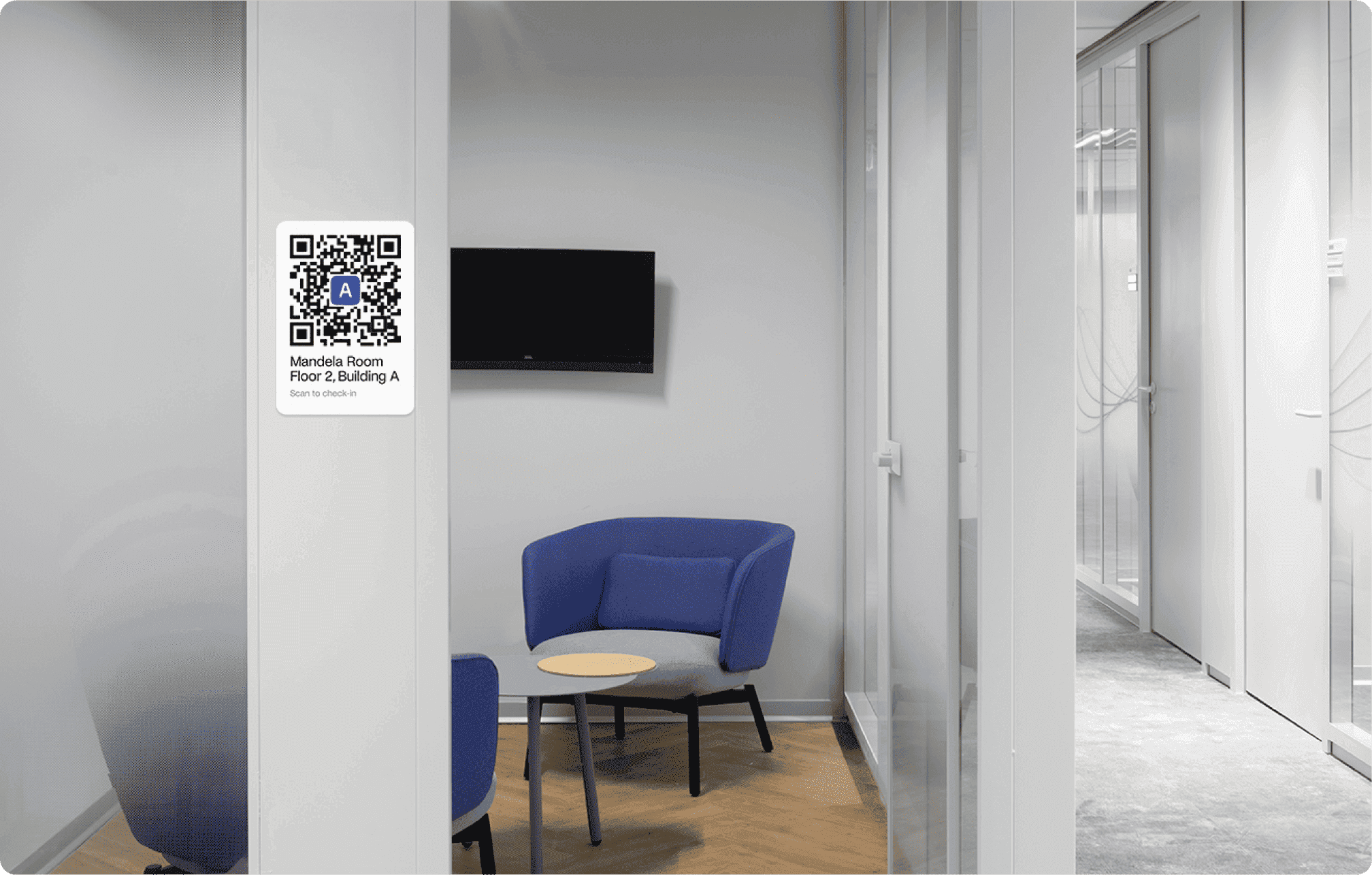Small meeting room with a QR code sign for check-in with the Archie app, a TV, and two blue chairs.