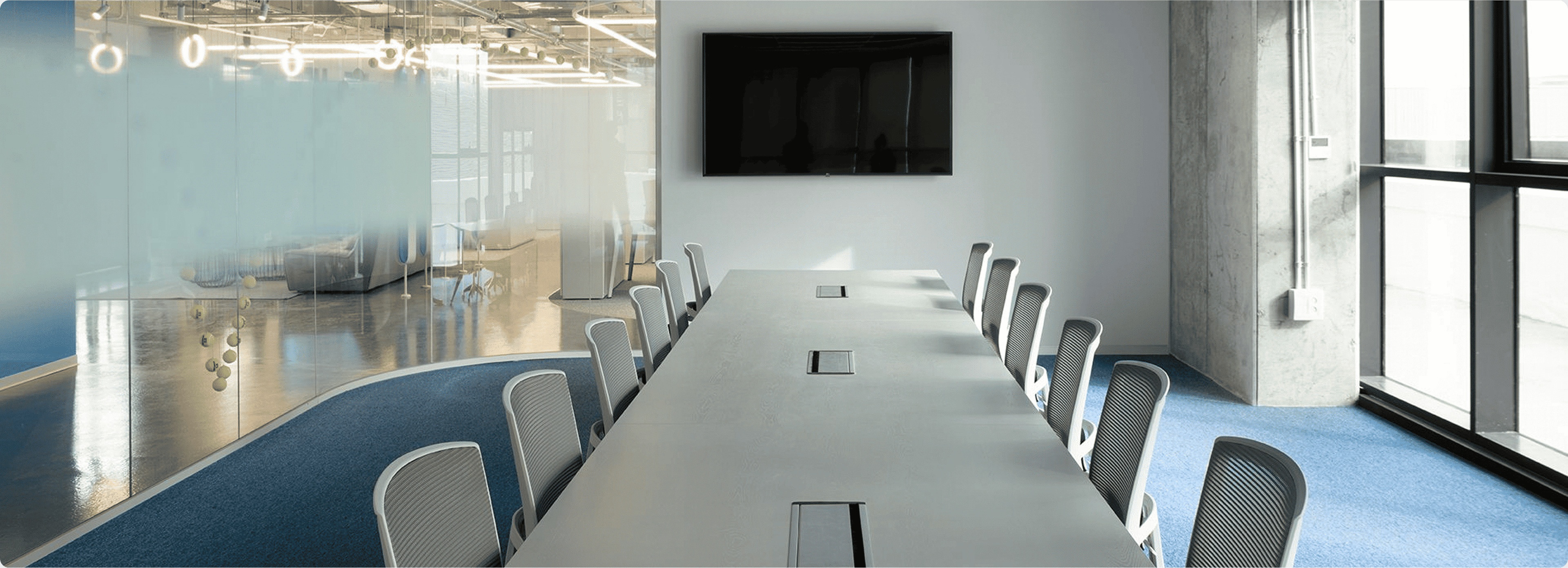 Modern conference room with a large table, chairs, and a TV mounted on the wall.